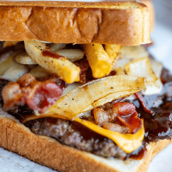 Close-up of a Busloop Burger with bacon, cheese, grilled onions, and fries on toasted bread.