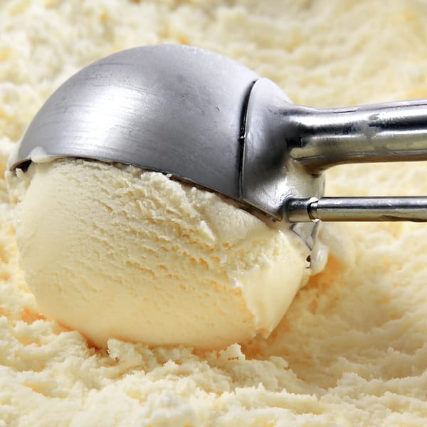 A metal ice cream scoop serving a large scoop of vanilla ice cream from a tub.