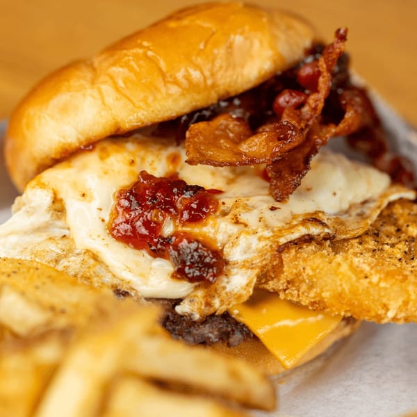 Busloop Burgers' burger with bacon, fried egg, hash brown, cheese, and jam, with fries.