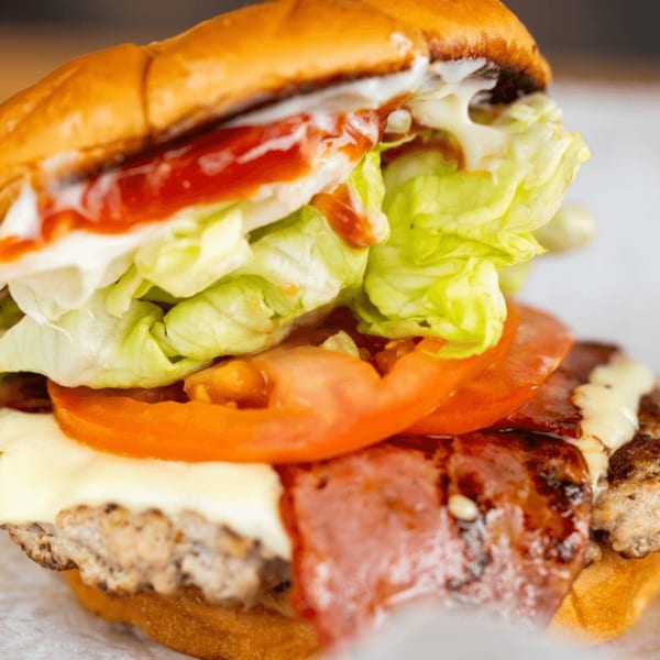 Close-up of a Busloop Burger with lettuce, tomato, cheese, bacon, and sauces on a bun.