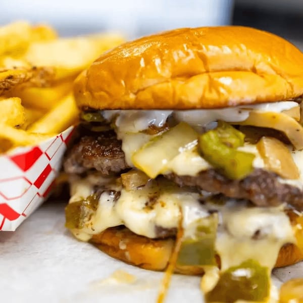 A double cheeseburger with melted cheese, grilled onions, and green peppers, next to fries.