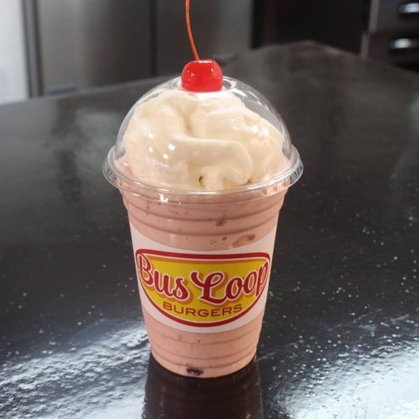 Busloop Burgers strawberry milkshake with whipped cream and a cherry on top, on a dark counter.
