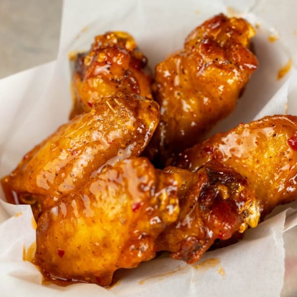 Close-up of several Busloop Burgers chicken wings, coated in a glistening orange sauce with specks of seasoning.