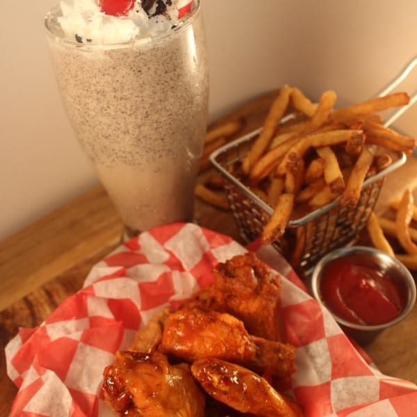 Busloop Burgers' chicken wings, fries, ketchup, and an Oreo milkshake on a wooden table.